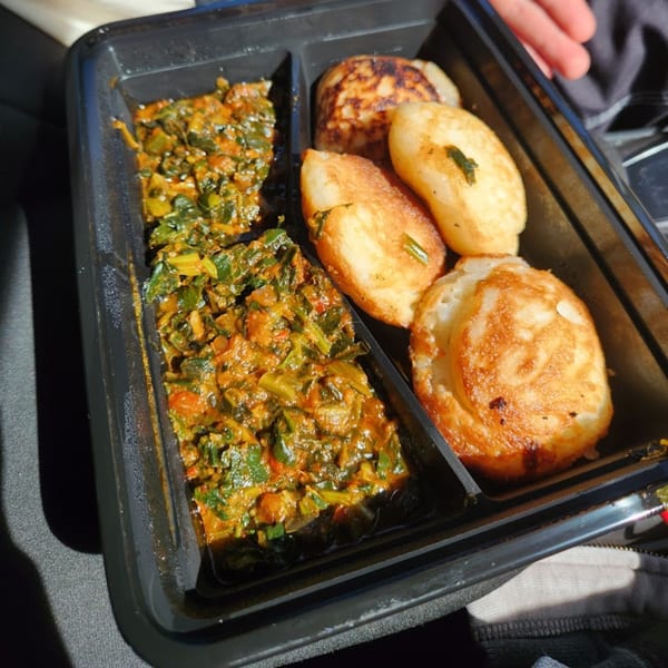 A black takeout container holds green stew and golden-brown fried dough balls from Lynda's African Delicacies.