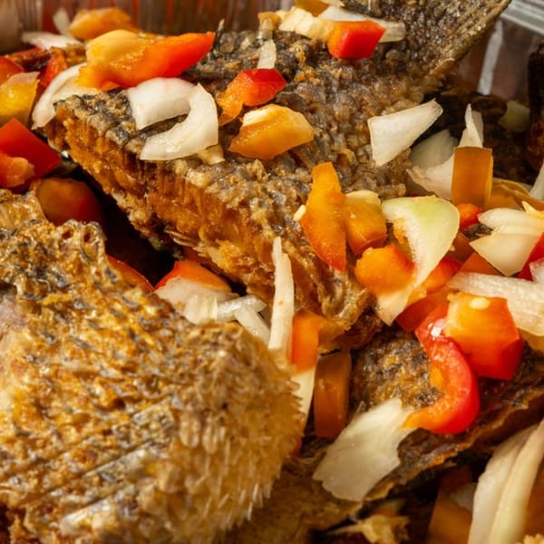 Crispy fried fish pieces topped with diced red peppers, yellow peppers, and white onions.