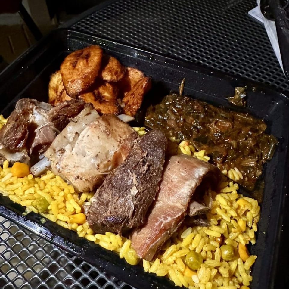 Lynda's African Delicacies meal with rice, meat, plantains, and greens in a black container.